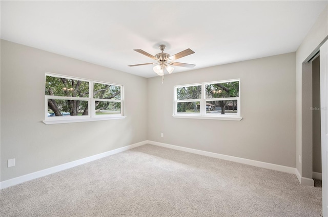 carpeted spare room with a healthy amount of sunlight, a ceiling fan, and baseboards