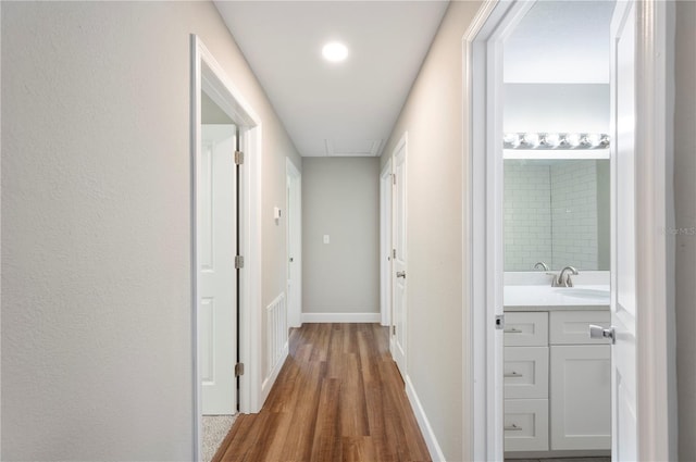 hall with wood finished floors, baseboards, and a sink