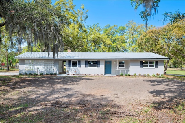 ranch-style home featuring concrete block siding, a chimney, covered porch, and metal roof