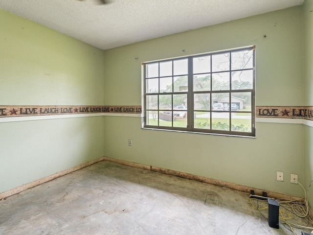 empty room with a wealth of natural light, baseboards, a textured ceiling, and unfinished concrete floors