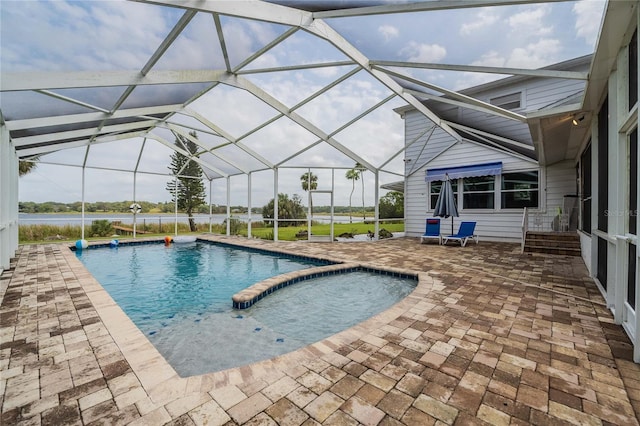 view of swimming pool featuring glass enclosure, a water view, a pool with connected hot tub, and a patio area