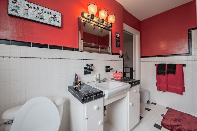 half bathroom featuring toilet, tile walls, wainscoting, tile patterned flooring, and vanity