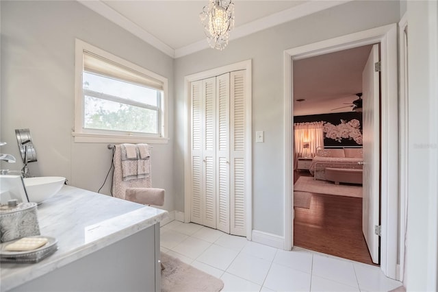 laundry room with ornamental molding, ceiling fan with notable chandelier, a sink, light tile patterned flooring, and baseboards