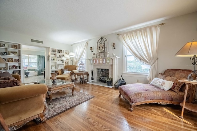 living area featuring visible vents, a fireplace with flush hearth, a textured ceiling, and wood finished floors