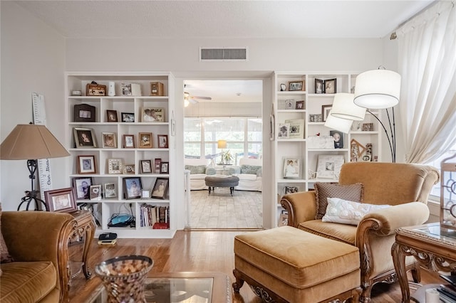 sitting room with ceiling fan, visible vents, a textured ceiling, and wood finished floors