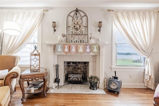 living area featuring a tiled fireplace, baseboards, and wood finished floors