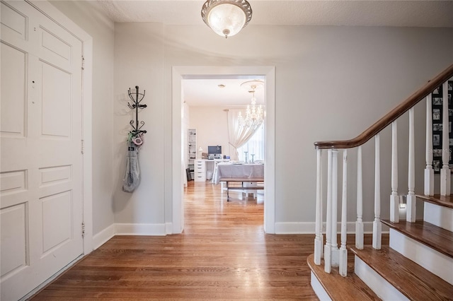 foyer with stairway, baseboards, an inviting chandelier, and wood finished floors