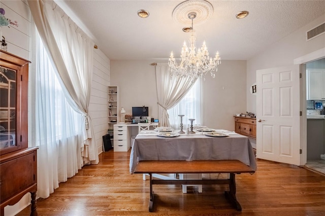 dining area featuring visible vents, an inviting chandelier, a textured ceiling, and light wood-style floors