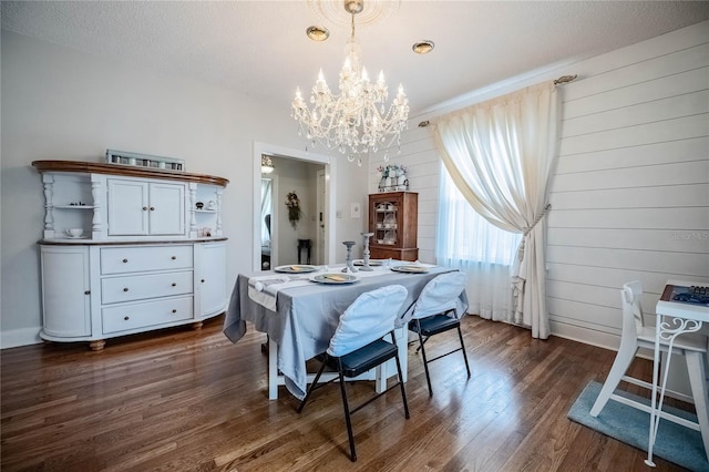 dining space featuring dark wood-style floors, a notable chandelier, wood walls, and a textured ceiling