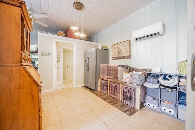 interior space with a wall mounted air conditioner, decorative light fixtures, stainless steel fridge, and light tile patterned floors