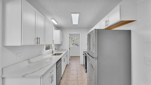 kitchen with light stone counters, light tile patterned floors, a sink, stainless steel appliances, and white cabinets