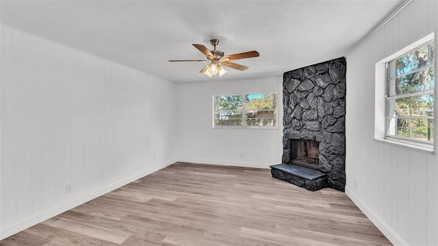 unfurnished living room featuring light wood finished floors, a stone fireplace, baseboards, and ceiling fan