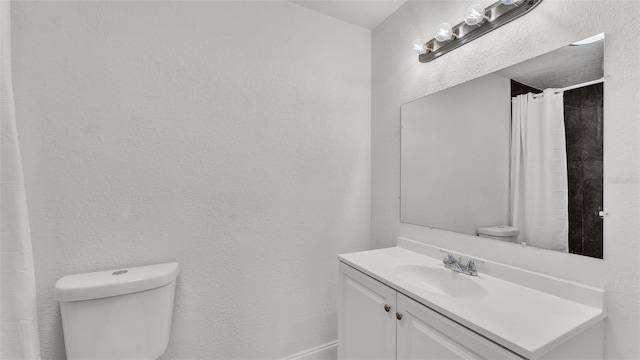 full bath featuring vanity, toilet, and a textured wall