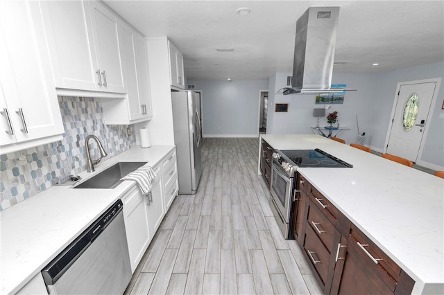 kitchen with backsplash, appliances with stainless steel finishes, island exhaust hood, white cabinets, and a sink