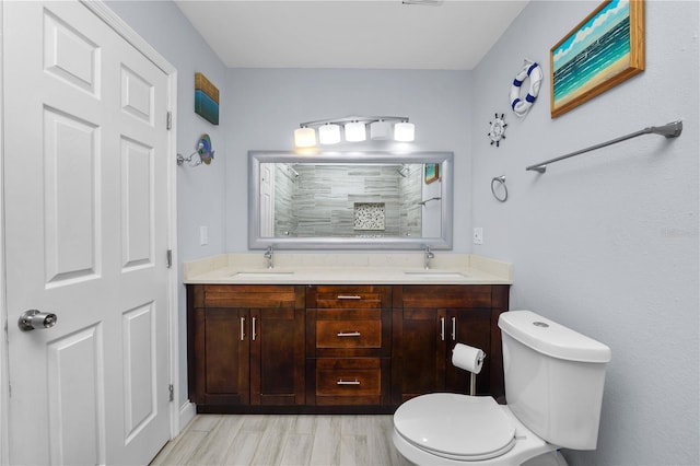 bathroom featuring double vanity, tiled shower, toilet, and a sink