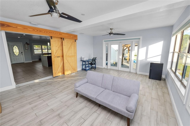 living area featuring a wealth of natural light, a barn door, light wood-style flooring, and a ceiling fan