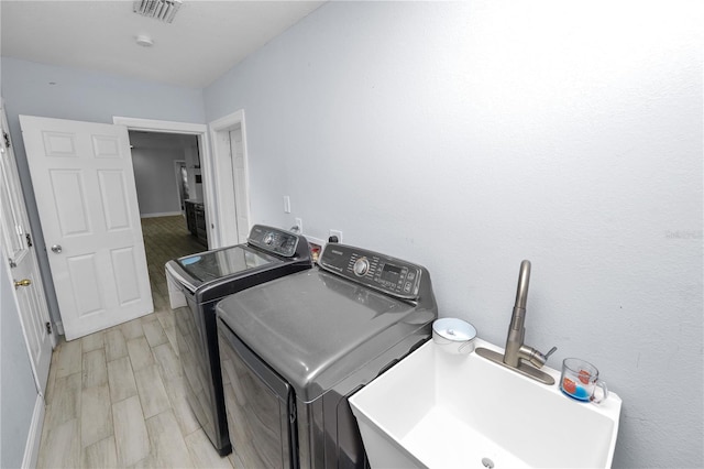 laundry room featuring visible vents, laundry area, separate washer and dryer, a sink, and light wood-type flooring