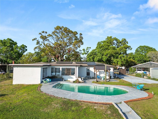 rear view of property featuring fence, a yard, an outdoor pool, stucco siding, and roof mounted solar panels