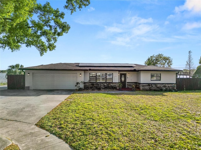 view of front of home featuring stucco siding, a front lawn, roof mounted solar panels, fence, and a garage