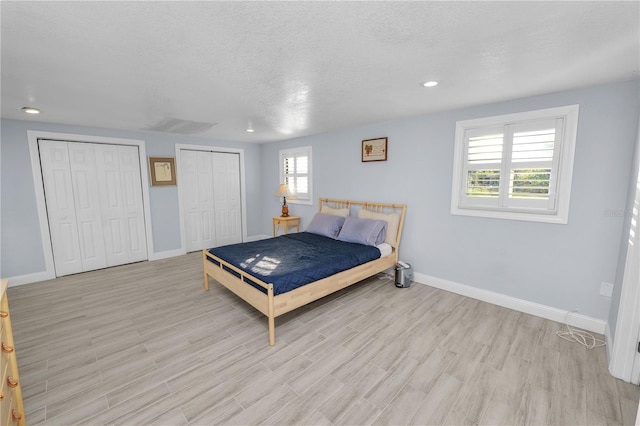 bedroom with a textured ceiling, baseboards, multiple closets, and light wood-type flooring