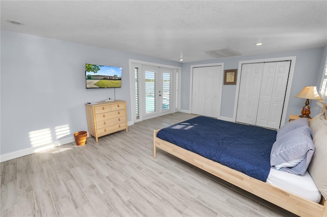 bedroom with access to exterior, multiple closets, french doors, light wood-style floors, and a textured ceiling