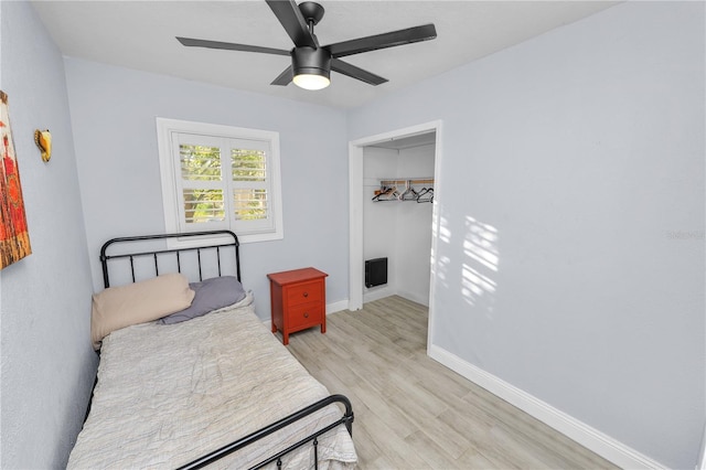 bedroom with light wood finished floors, a walk in closet, ceiling fan, baseboards, and a closet