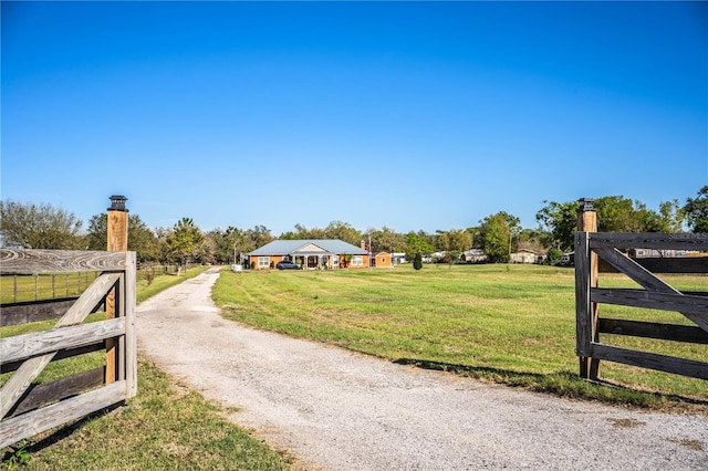 view of gate with a rural view, fence, and a lawn