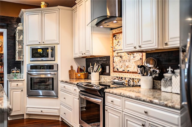 kitchen featuring dark wood-type flooring, tasteful backsplash, stainless steel appliances, wall chimney range hood, and light stone countertops