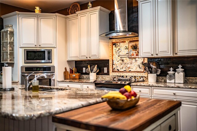 kitchen featuring a sink, appliances with stainless steel finishes, wall chimney exhaust hood, decorative backsplash, and light stone countertops