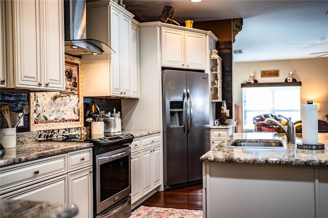 kitchen featuring wall chimney range hood, light stone countertops, decorative backsplash, appliances with stainless steel finishes, and a sink