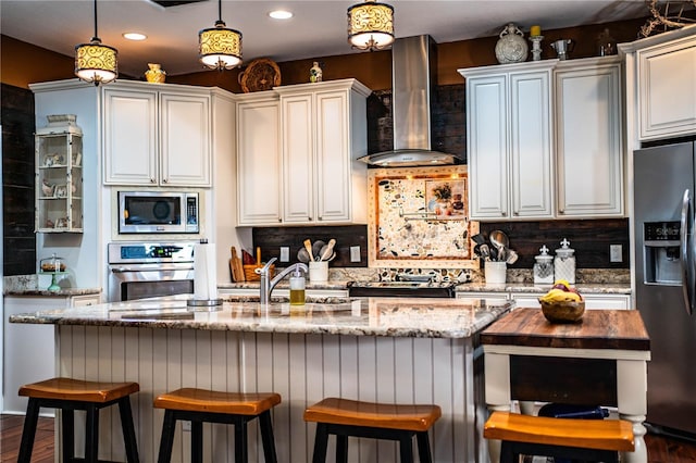 kitchen featuring decorative light fixtures, a sink, backsplash, stainless steel appliances, and wall chimney exhaust hood