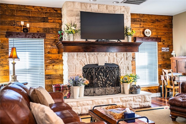 living area featuring a stone fireplace, wooden walls, wood finished floors, and visible vents