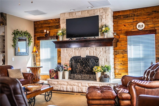 carpeted living room with wooden walls, a fireplace, and visible vents