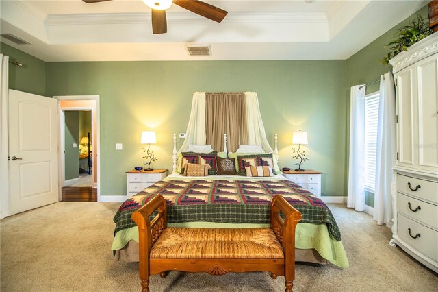 bedroom featuring a tray ceiling, visible vents, light colored carpet, and crown molding