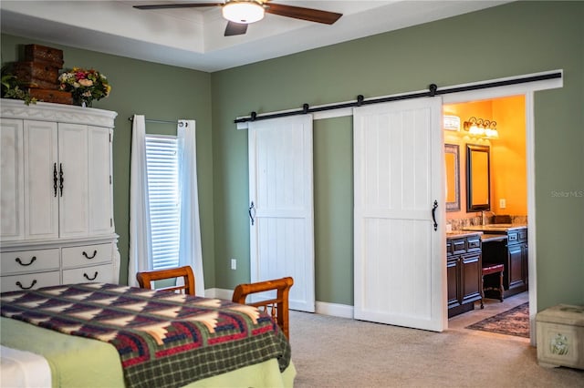 bedroom featuring a barn door, light carpet, ensuite bath, a raised ceiling, and a ceiling fan