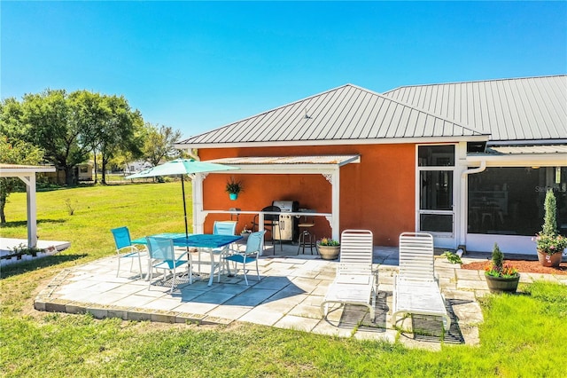 back of property with a patio, stucco siding, a yard, and metal roof