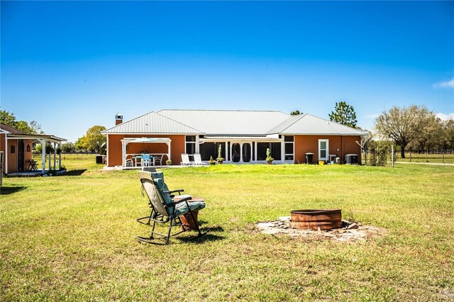 rear view of property with a chimney, an outdoor fire pit, and a yard