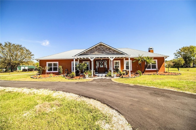 view of front facade with a front lawn, a porch, a chimney, metal roof, and a standing seam roof