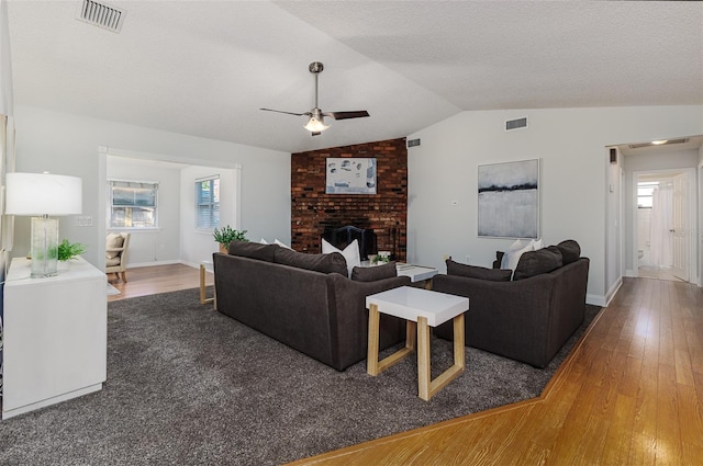 living area featuring visible vents, hardwood / wood-style floors, lofted ceiling, a brick fireplace, and ceiling fan