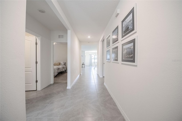 hall featuring visible vents, baseboards, and light tile patterned flooring