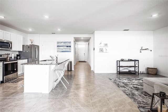 kitchen with a kitchen island with sink, a sink, stone countertops, a kitchen breakfast bar, and stainless steel appliances