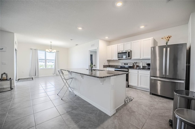 kitchen with light tile patterned flooring, a sink, stainless steel appliances, white cabinets, and a kitchen bar