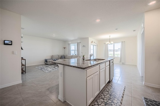 kitchen featuring a sink, dark stone counters, light tile patterned floors, dishwashing machine, and a kitchen island with sink