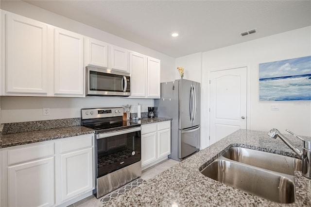 kitchen with visible vents, a sink, dark stone countertops, appliances with stainless steel finishes, and white cabinets