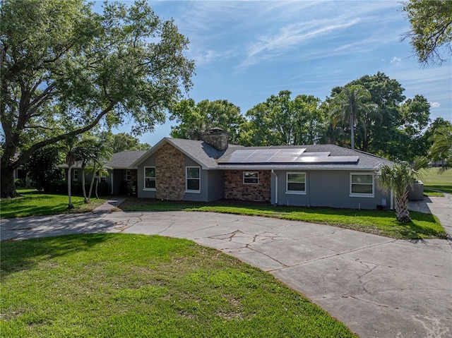 single story home featuring stucco siding, curved driveway, a front yard, solar panels, and a chimney