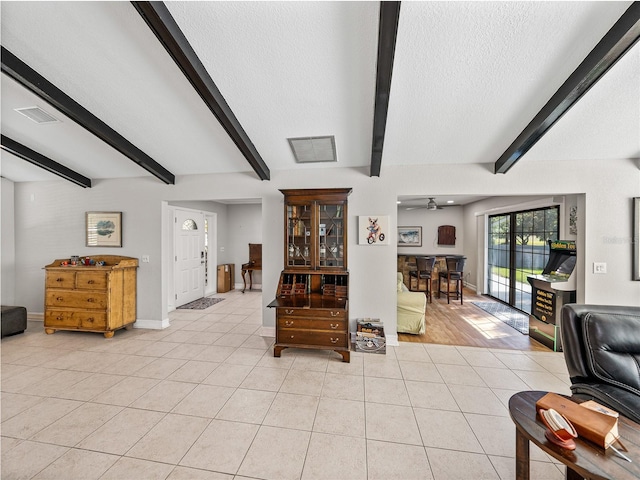living room featuring beam ceiling, light tile patterned floors, visible vents, and a textured ceiling