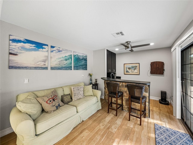 living room featuring baseboards, a ceiling fan, visible vents, and light wood-type flooring