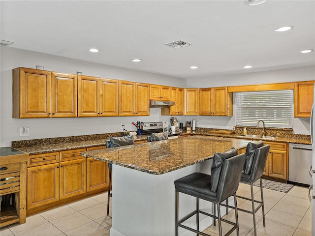 kitchen featuring visible vents, a breakfast bar, stainless steel appliances, a sink, and under cabinet range hood