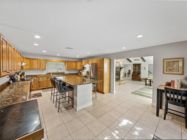 kitchen featuring a center island, stainless steel appliances, a breakfast bar area, a fireplace, and light tile patterned floors