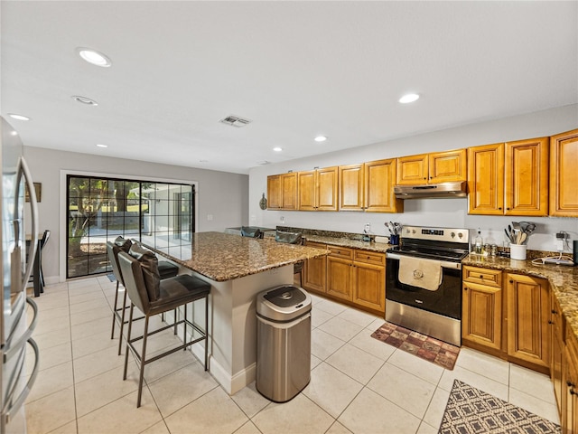 kitchen featuring visible vents, under cabinet range hood, a kitchen breakfast bar, dark stone counters, and appliances with stainless steel finishes